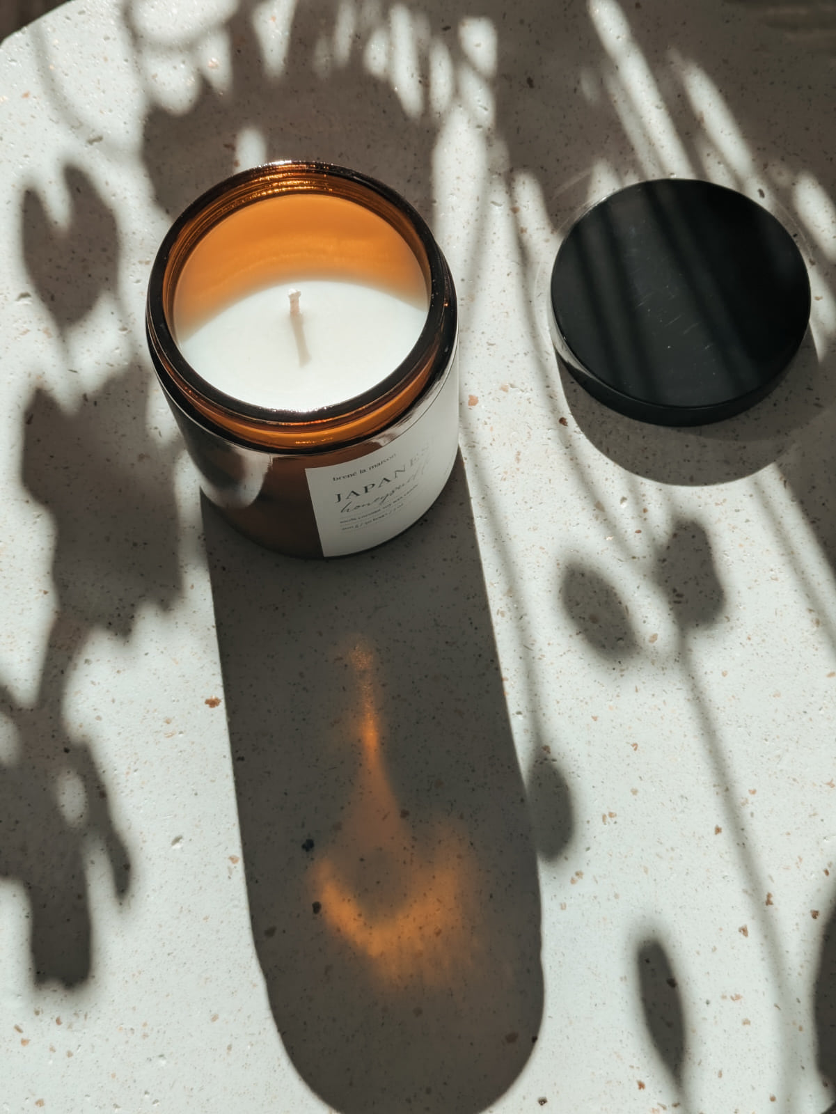 Japanese Honeysuckle candle, open jar with lid beside, top-down dappled light